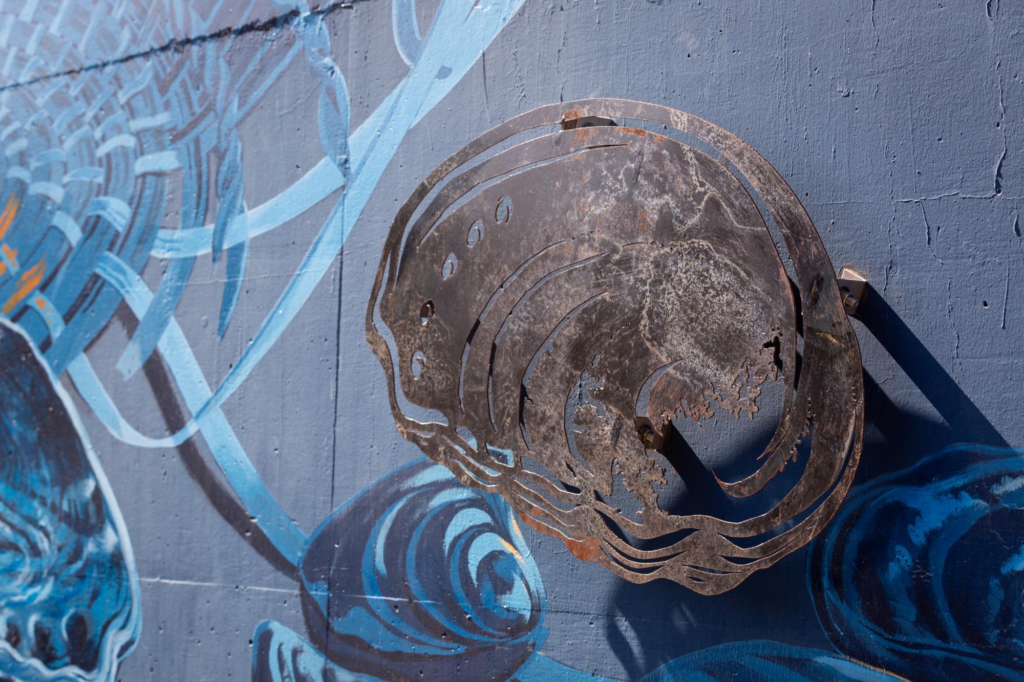 Metal cutout of an abolone shell installed against blue mural backdrop.